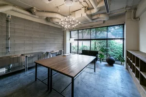 A modern conference room featuring a wooden table, concrete walls, and stainless steel fixtures, with a view of greenery outs