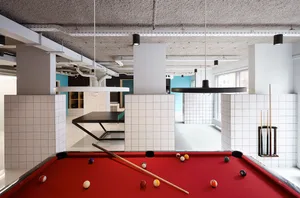 Industrial-style pool hall with a red felt pool table, white tile walls, concrete pillars, and billiard balls placed on the t