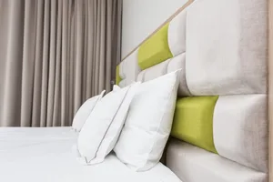 A minimalist bedroom with a fabric headboard featuring green accents and white pillows.