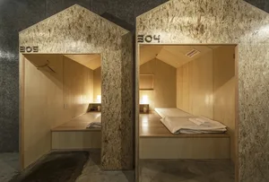 A minimalist bedroom with wooden walls, a single bed, and simple lighting fixtures.