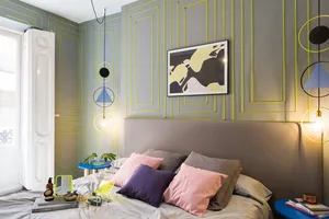A modern bedroom featuring geometric wall designs and various cushions on the bed.