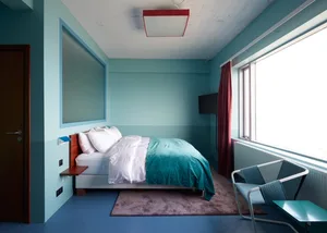 A modern minimalist bedroom featuring a blue-green color scheme with a bed, chair, and window.