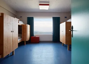 Minimalist bedroom with wooden cabinets, blue floor tiles, and a view of the sea through the window.