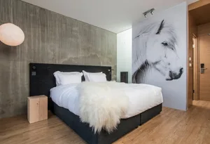 Modern minimalist bedroom featuring a black bed with white bedding, a white fur throw, and a large black and white horse wall