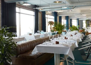 A modern restaurant interior filled with green plants and white tables.
