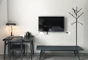 A minimalistic hotel room with a black desk, black bench, and a mounted television on the wall.