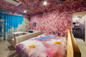 A modern bedroom with floral print walls, ceiling, and bedding, featuring a white sofa and a bed with a floral comforter.
