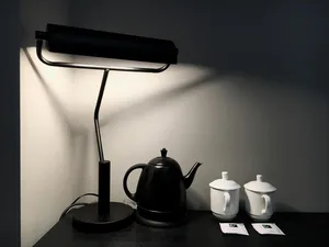 Modern coffee station featuring a ceramic matte black kettle and two matching cups, with a sleek black desk lamp casting ligh
