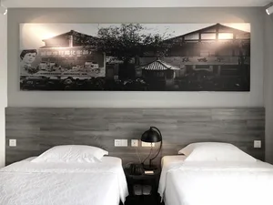 A modern hotel room features a wooden headboard with two twin beds, white linens, and a black lamp on a side table.