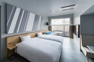 A minimalist hotel room with neutral tones, featuring two twin beds, a large window, and modern furnishings.