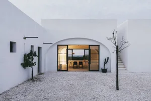 A minimalist white building with large windows and a gravel courtyard.