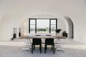 A modern industrial dining room with cement walls, wooden table, and black chairs and accents.