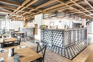 Modern restaurant interior with wooden tables, geometric-patterned tile flooring, and metallic accents.