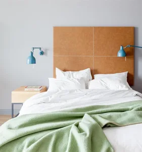 Minimalist bedroom with a bed featuring a green blanket, white sheets, and a brown leather headboard.