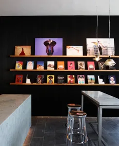A photograph of an art gallery featuring shelves filled with colorful paintings, a marble countertop, and stools.