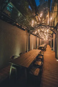 Modern, industrial-looking restaurant exterior with wooden tables, metal chairs, and glass ceiling.