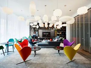 A mid-century modern living room with colorful cone-shaped chairs, a black sofa, and hanging white pendant lights.