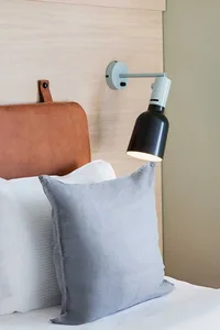 A minimalist bedroom with a gray cushion, a leather headboard, and a modern lamp on the wall.