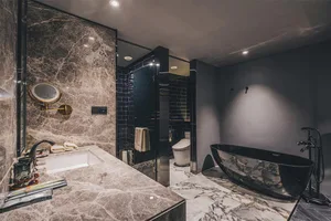 A modern bathroom featuring a marble sink, black bathtub, and black tiles.