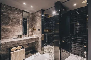 Modern bathroom with marble walls and floor, sink, mirror, and tiled shower area.
