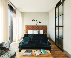 Modern bedroom featuring a green velvet sofa, a tufted leather headboard bed, and a wooden coffee table with books.