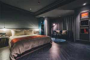 Modern hotel room featuring dark timber flooring and a comfortable bed with plush pillows and a colorful blanket.