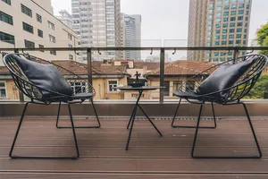 Modern industrial chairs with black metal framing and cushions on a wooden deck with a cityscape background.