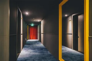 A modern hallway with glass panels, lighting fixtures, and carpeted flooring, featuring a reflection on a glass wall.