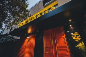 Modern metal storefront with a yellow neon sign reading "THE DRAMA"