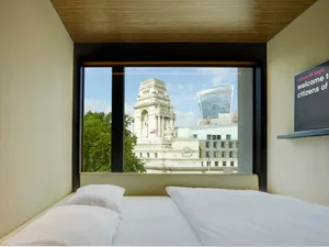 A modern hotel room pod overlooking a historic and modern cityscape through a large glass window.