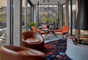 Modern retail storefront with orange leather chairs, glass tables, concrete columns, and plants.