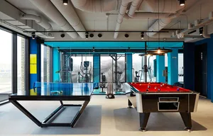 Modern, industrial-style gym with table tennis and pool tables, fitness equipment, and large windows for natural light.