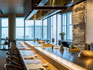 Modern industrial-style restaurant interior with wooden seating and glass walls showing a cityscape.