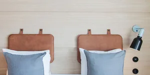 A minimalist bedroom with blue pillows on a bed, against a light-colored wooden headboard.