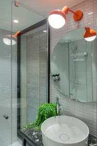 Modern bathroom with concrete and ceramic tiles, round sink, orange lights, and green plant.