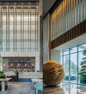 A modern hotel lobby featuring a wooden sphere sculpture and a large glass wall