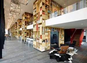 Modern, wooden bookshelves surrounded by comfortable seating areas in a large, open space with a circular light fixture hangi