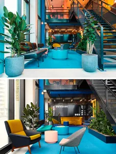 A modern office lounge area with concrete elements, indoor plants, and carpeted floors.