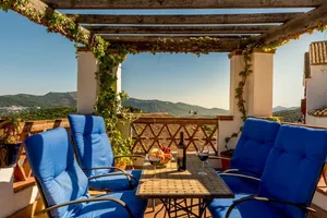 Outdoor lounge area with blue cushioned chairs, wooden pergola, and scenic mountain view.
