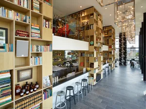 A modern coffee bar with wooden shelves filled with books and a marble counter.