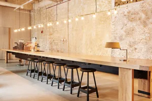 Industrial-style coffee shop interior featuring a long wooden counter with black stools and gold lighting fixtures.