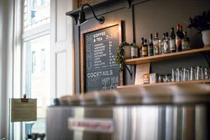 A metal sign displaying a coffee shop's menu, including coffee and tea items, cocktails, draft beer, and wine.