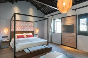 A modern bedroom featuring a bed with a black metal frame, wood headboard, and textiles, illuminated by hanging lantern-style