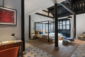 A modern bedroom featuring a desk, floor tiles with triangular patterns, and a large bed with a canopy frame.