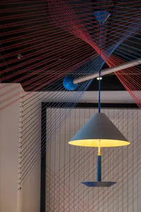 A modern light fixture hanging from the ceiling, surrounded by textile strings