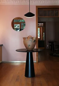 Modern entrance hall featuring a black cylindrical table with a round top, displaying a large, abstract ceramic vase with a h