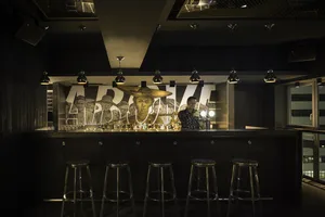 Industrial-style bar with concrete countertop, hanging lights, and metal stools in a modern setting.