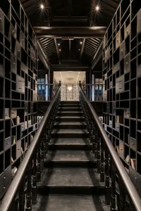 An indoor staircase surrounded by metal shelves filled with books, leading to a brightly lit area.