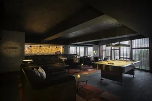 An industrial lounge area featuring a concrete wall, leather sofas, and a wooden pool table.
