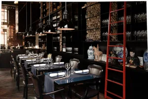 A modern industrial restaurant interior featuring metal pendant lights, wooden chairs, and glassware.